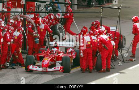 (dpa) - Ferrari mechanics rush towards Brazilian formula one pilot Rubens Barrichello (Ferrari) (front) who sits in his racing car while behind him stands his teammate German formula one world champion Michael Schumacher (back, covered) awaiting assistance at the pit-stop pumping station during the British Grand Prix formula one race in Silverstone, UK, 20 July 2003. Schumacher fel Stock Photo