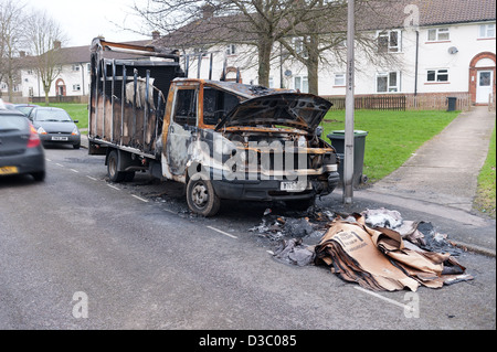 burnt vandalized van near end of grass verge footpath leading to white painted rendered terraced housing