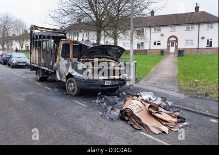 burnt vandalized van near end of grass verge footpath leading to white painted rendered terraced housing