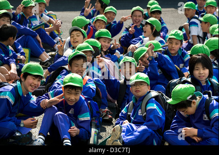 Smiling happy faces of Japanese elementary school boys and girls wearing colorful green caps and flashing the peace sign. Stock Photo