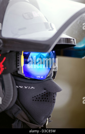 Man wearing protective headgear, face mask and reflective goggles while riding a snowmobile Stock Photo