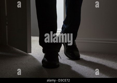 Man entering a dark room, backlit shot of legs and feet only. Close up. Stock Photo