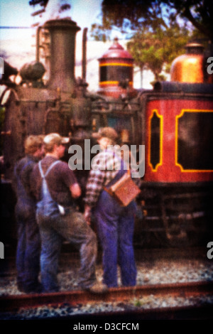 A vintage old style photo of a group of engine drivers and railway workers standing beside an old working steam train. Stock Photo