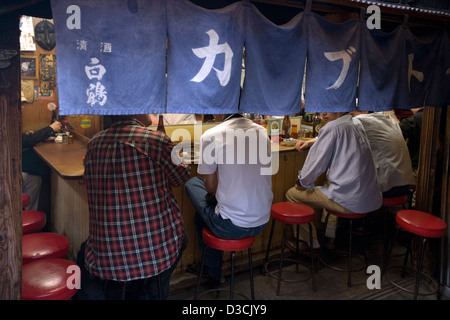 Patrons behind a noren curtain enjoy good food and friendship at counter eatery restaurant in Omoide Yokocho, Memory Lane, Tokyo Stock Photo