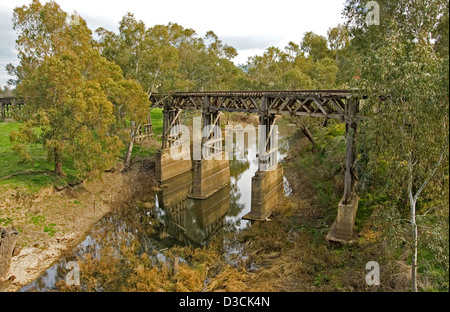 Historic wooden trestle railway bridge through woodland and reflected in calm water of narrow stream far below at Gundagai, NSW Stock Photo