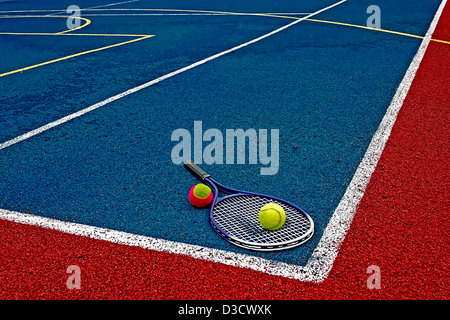 Tennis colored balls and racket, placed in the corner of a synthetic field. Stock Photo
