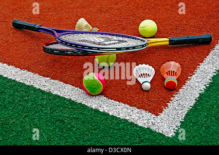 Badminton colored shuttlecocks with tennis balls and rackets, placed in the corner of a synthetic field. Stock Photo