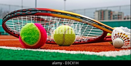Tennis colored balls, badminton shuttlecocks and rackets, placed in the corner of a synthetic field. Stock Photo
