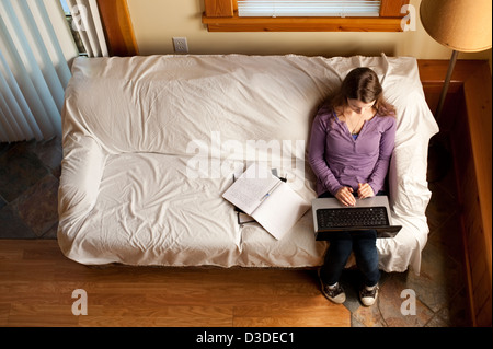 Young college student studying on couch using a computer and taking notes Stock Photo