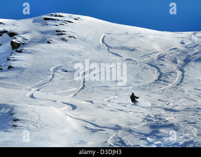 Snowboarder and off-piste tracks on snow in sunset light Stock Photo