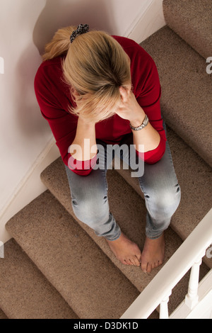 Woman with blond hair, head in her hands. Sitting on the stairs, viewed from above. Stock Photo