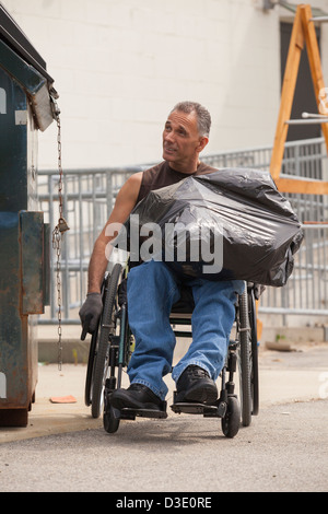 Loading dock worker with spinal cord injury in a wheelchair putting a bag in the dumpster Stock Photo