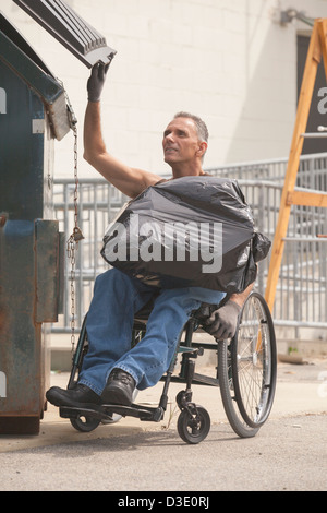 Loading dock worker with spinal cord injury in a wheelchair putting a bag in the dumpster Stock Photo