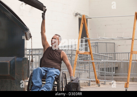 Loading dock worker with spinal cord injury in a wheelchair putting a bag in the dumpster Stock Photo