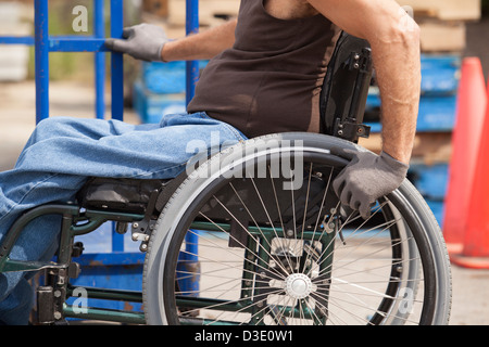 Loading dock worker with spinal cord injury in a wheelchair moving a hand truck Stock Photo