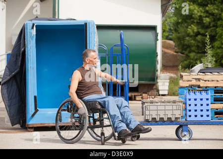 Loading dock worker with spinal cord injury in a wheelchair moving a hand truck Stock Photo