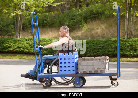 Loading dock worker with spinal cord injury in a wheelchair moving a hand truck Stock Photo