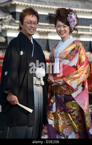 A happy bride and groom wearing traditional wedding kimono as they pose in front of Matsumoto Castle in Nagano. Stock Photo