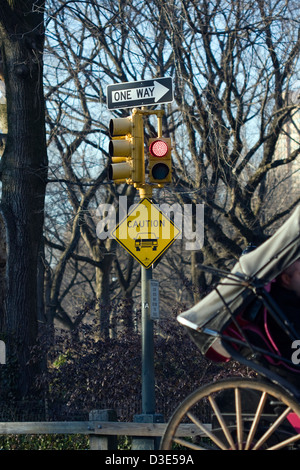 Horse Drawn Carriage rolls past a 'Caution Motor Vehicle' sign below a traffic light on the East Dr. in New York's Central Park Stock Photo