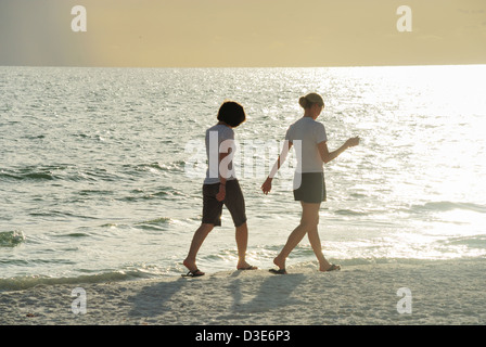 Two young women walk on beach into glow from setting sun Stock Photo
