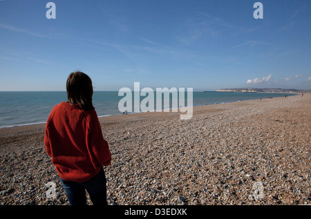 Back to camera shot of a woman wearing a chunky men's jumper looking out to sea, signifying loss of a loved one. Stock Photo