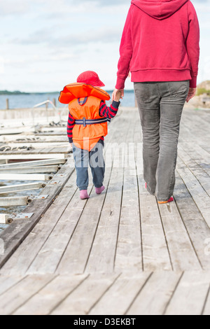 Mother holding the hand of her young child on a wooden jetty by the sea Stock Photo