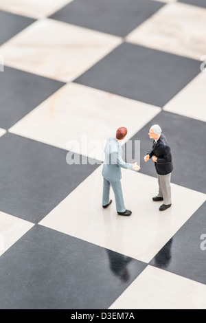 Two small figurines of businessmen standing on chessboard shaking hands Stock Photo