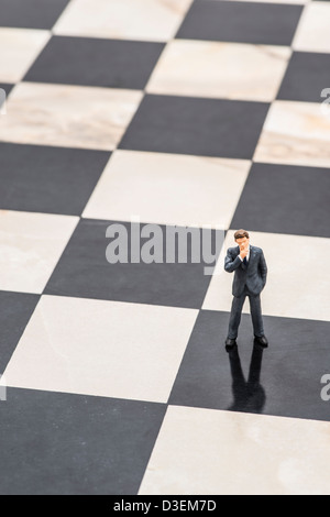 Small figurine of businessman standing on chessboard and thinking of strategic planning Stock Photo