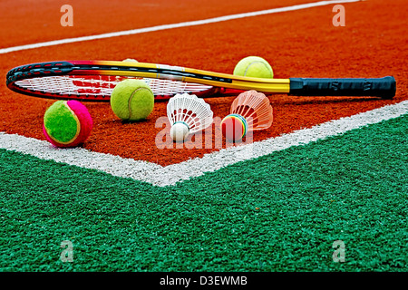 Badminton colored shuttlecocks with tennis balls and rackets, placed in the corner of a synthetic field. Stock Photo