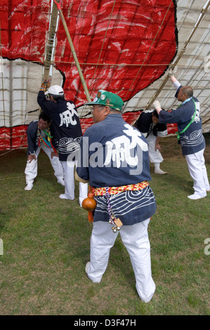 Team wearing happi coats hold up paper and bamboo kite for assembly at Sagami no Otako Matsuri Giant Kite Festival in Japan Stock Photo