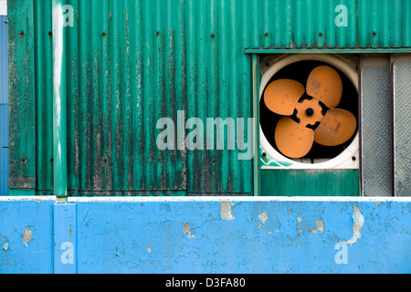 Simple, colorful composition of bright green siding, blue concrete wall and an orange ventilation fan on factory wall in Japan Stock Photo