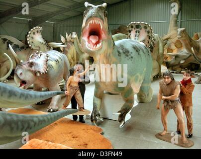 (dpa) - Two employees move the figures of stone age people standing next to a life-size dinosaur model in the hall of a large-size sculpture company in Loccum, Germany, 19 November 2004. The company has specialised in manufacturing replications of prehistoric animals which are sold or rented to museums and exhibitions worldwide. The light sculptures are made of plastic and easy to  Stock Photo