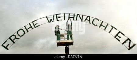 (dpa) - Two workers fit the writing 'Frohe Weihnachten' (Merry Christmas) in the shape of a light installation on the market place in Haldensleben, Germany, 22 November 2004. Stock Photo