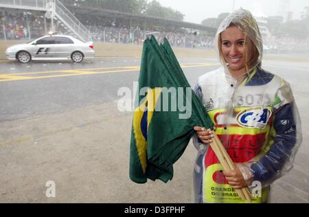 (dpa) - In the pouring rain a helper in a raincoat stands with soaked Brazilian flags on the formula one race track of Interlagos in Sao Paulo, Brazil, 6 April 2003. In the background a safety car drives through the pit lane. Due to heavy rainfalls the track was partly flooded, causing several accidents and ten drivers to drop out. The Grand Prix of Brazil was finally stopped on la Stock Photo