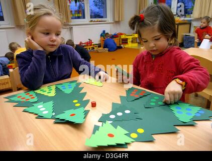 (dpa) - The three-year-old Bentje (R) and six-year-old Hannah play with paper Christmas trees bearing one to six dots at the daycare kindergarten centre in Pokrent, Germany, 28 November 2003. Stock Photo