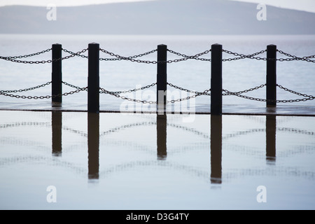 Fence reflected in a pool of water with the sea in the background. Stock Photo