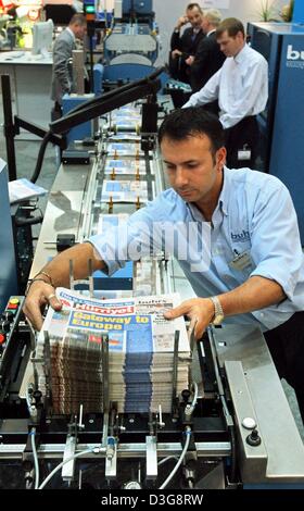 (dpa) - Francisco Exposito of the company Buhrs puts a stack of newspapers onto a conveyer belt of a machine which automatically wraps the stack with a plastic cover, at the Ifra-Expo newspaper fair in Leipzig, Germany, 13 October 2003. At the world's largest newspaper fair 307 companies from 18 countries will show their products from the newspaper and media publishing sector until Stock Photo