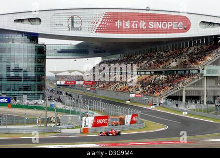 (dpa) - German Formula 1 driver Michael Schumacher (team Ferrari) races through the first curve at the new Shanghai International Circuit in Shanghai, China, 24 September 2004. In the background the start area and the main grandstand can be seen. The Chinese Grand Prix, the first ever Formula One race on Chinese soil, will take place on Sunday, 26 September 2004. Stock Photo