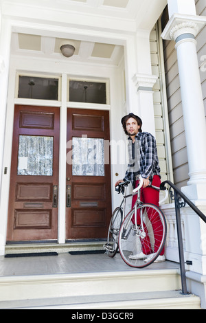 Hipsters and Beatniks - A young hipster man in tight jeans, plaid shirt, and hat about to leave home in his fixed-gear bike. Stock Photo