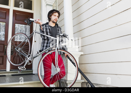 Hipsters and Beatniks - A young hipster man in tight jeans, plaid shirt, and hat about to leave home in his fixed-gear bike. Stock Photo