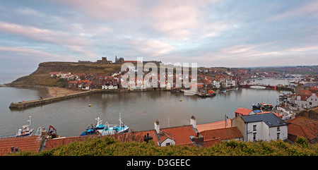 The town of Whitby in North Yorkshire looking above the rooftops across the harbour towards the Abbey ruins at dusk Stock Photo