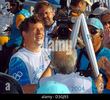 (dpa) - Otto Rehhagel (L), the German-born coach of the Greek national soccer team which won the Euro 2004 soccer championships, takes over the Olympic flame in Athens, 8 August 2004. Rehhagel will carry the flame over the Rio Antirio bridge in western Greece. The Olympic torch will arrive in Athens when the Games open on 13 August. Stock Photo