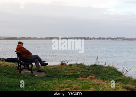 old elderly man lone single alone on own sit sitting bench look looking sea ocean think contemplate reminisce dusk sunset winter Stock Photo