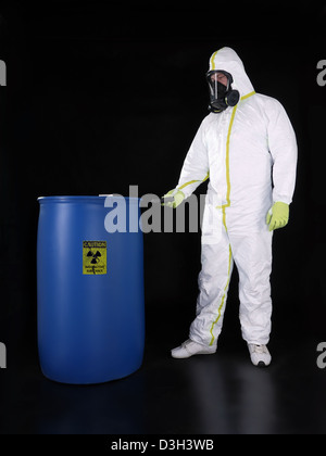 Man wearing protective suit checking radioactivity level of radioactive substance stored in blue container Stock Photo