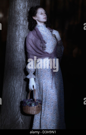 a woman is leaning against a trunk in dark woods Stock Photo