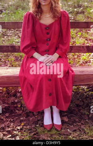 a woman in a red, rustic dress on a wooden bench Stock Photo