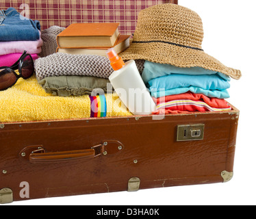 Old vintage suitcase packed with women's clothes, hat, books, sunglasses and beach towel Stock Photo