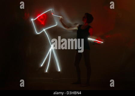 Artist female professional woman painter painting love red heart symbol on light canvas in darkness holding palette and a brush Stock Photo