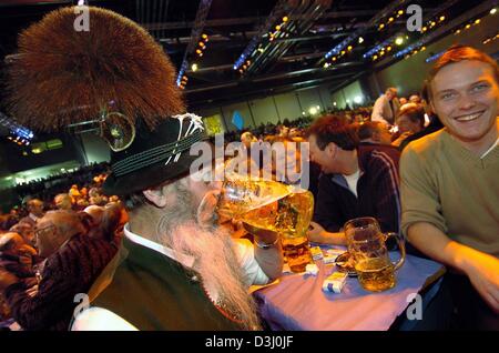 (dpa) - A beard man, dressed in traditional Bavarian clothing drinks from a beer glass while sitting opposit a young man who smiles during the traditional Ash Wednesday get-together of the CSU party in Passau, Germany, 25 February 2004.  The traditional event is a casual meeting among party members and supporters who amuse themselves by joking and laughing at last year's policies o Stock Photo