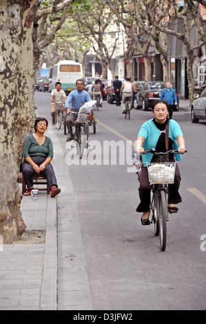 Chinese people riding bicycles in a street of the French Concession in Shanghai - China Stock Photo